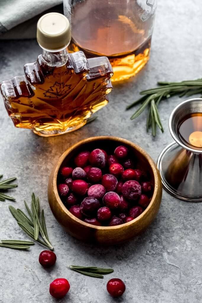 Bowl of cranberries next to container of maple syrup