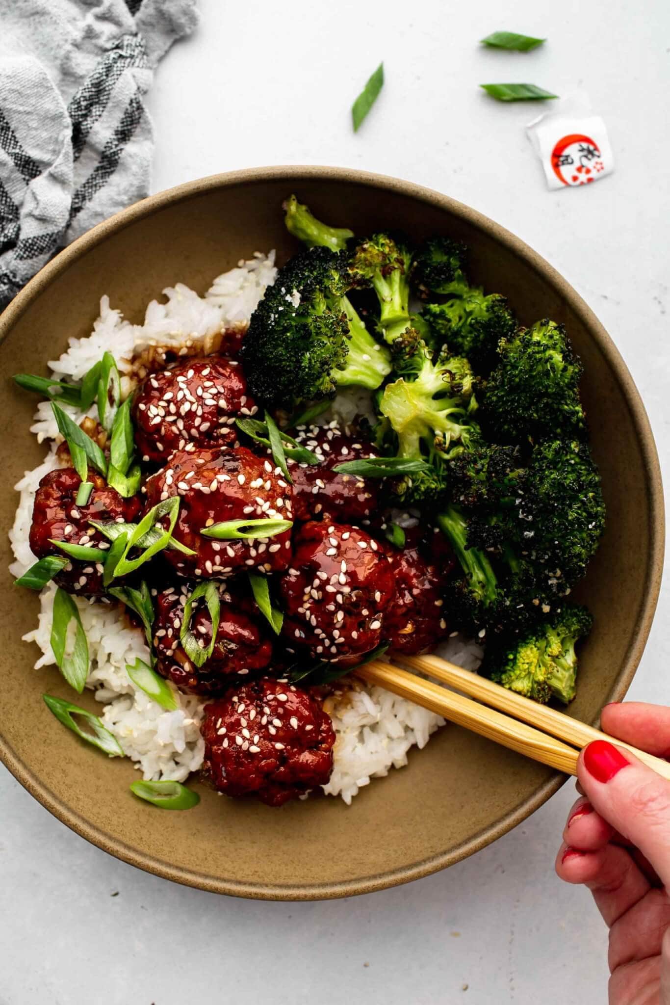 Hand holding chopsticks eating bowl of mongolian meatballs.