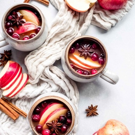 Overhead shot of three mugs of mulled cider next to apple slices.