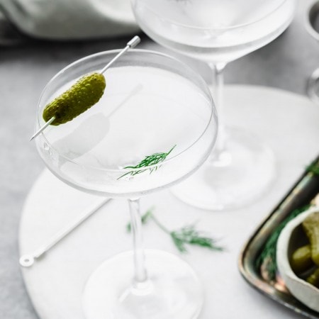 Side view of two pickle martinis garnished with small pickles.