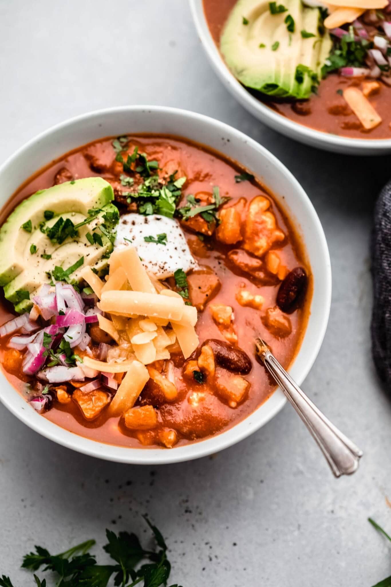 Bowl of pumpkin chili topped with cheese, avocado, sour cream and red onions. 