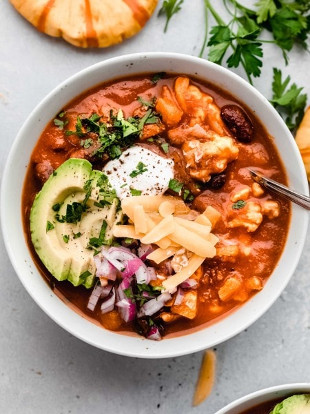 Bowl of pumpkin chili topped with cheese, avocado, sour cream and red onions.