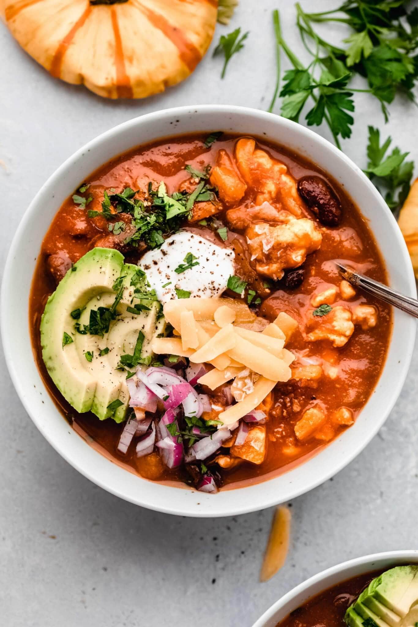 Bowl of pumpkin chili topped with cheese, avocado, sour cream and red onions.