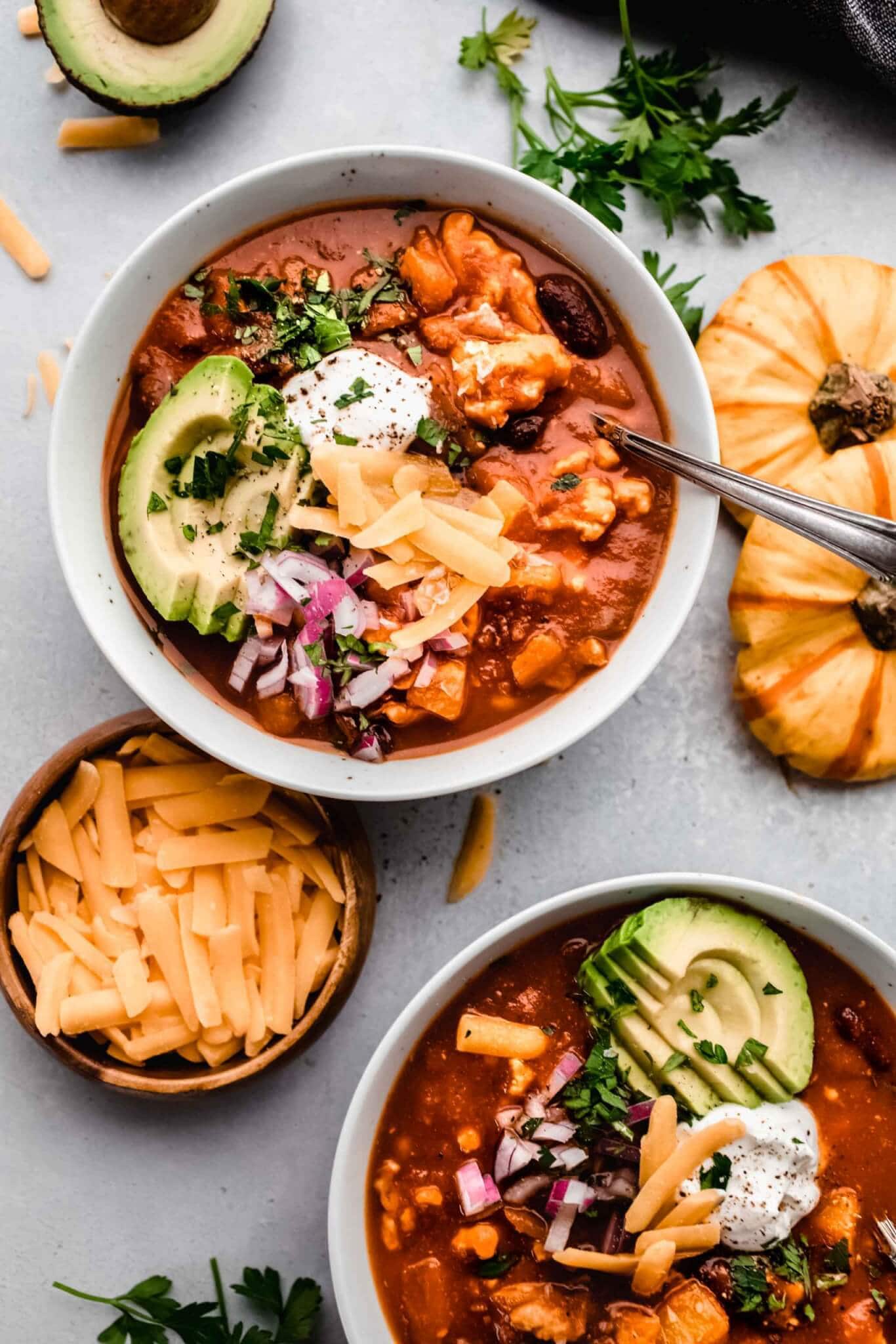 Bowl of pumpkin chili topped with cheese, avocado, sour cream and red onions. 