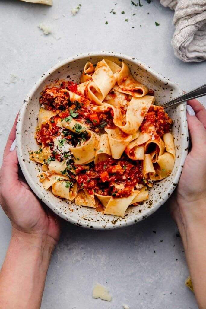 Hands holding bowl of pasta topped with slow cooker bolognese.