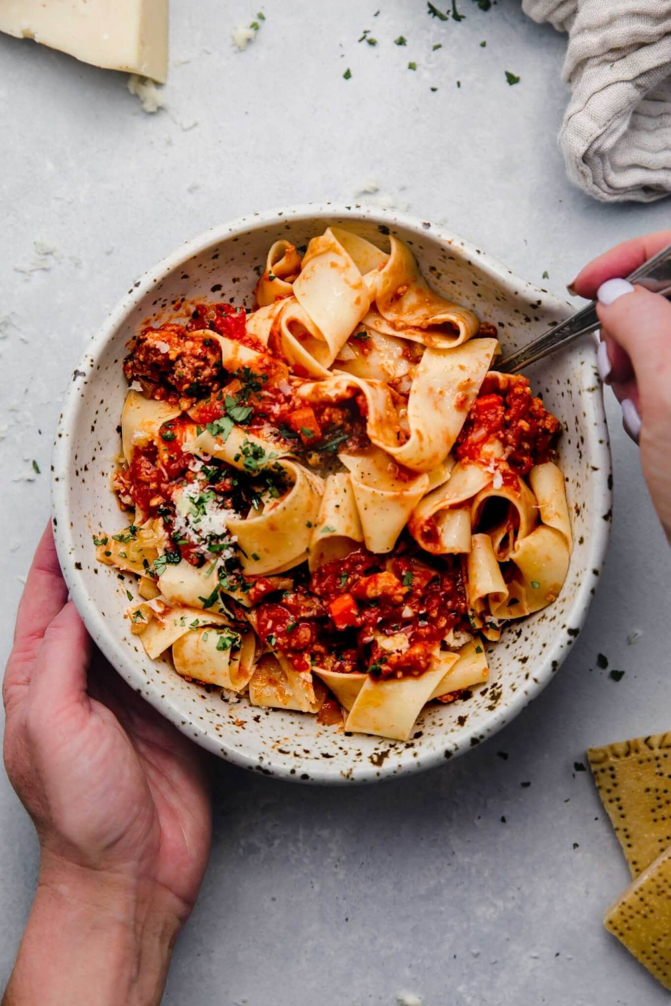 Hands holding bowl of pasta topped with slow cooker bolognese.