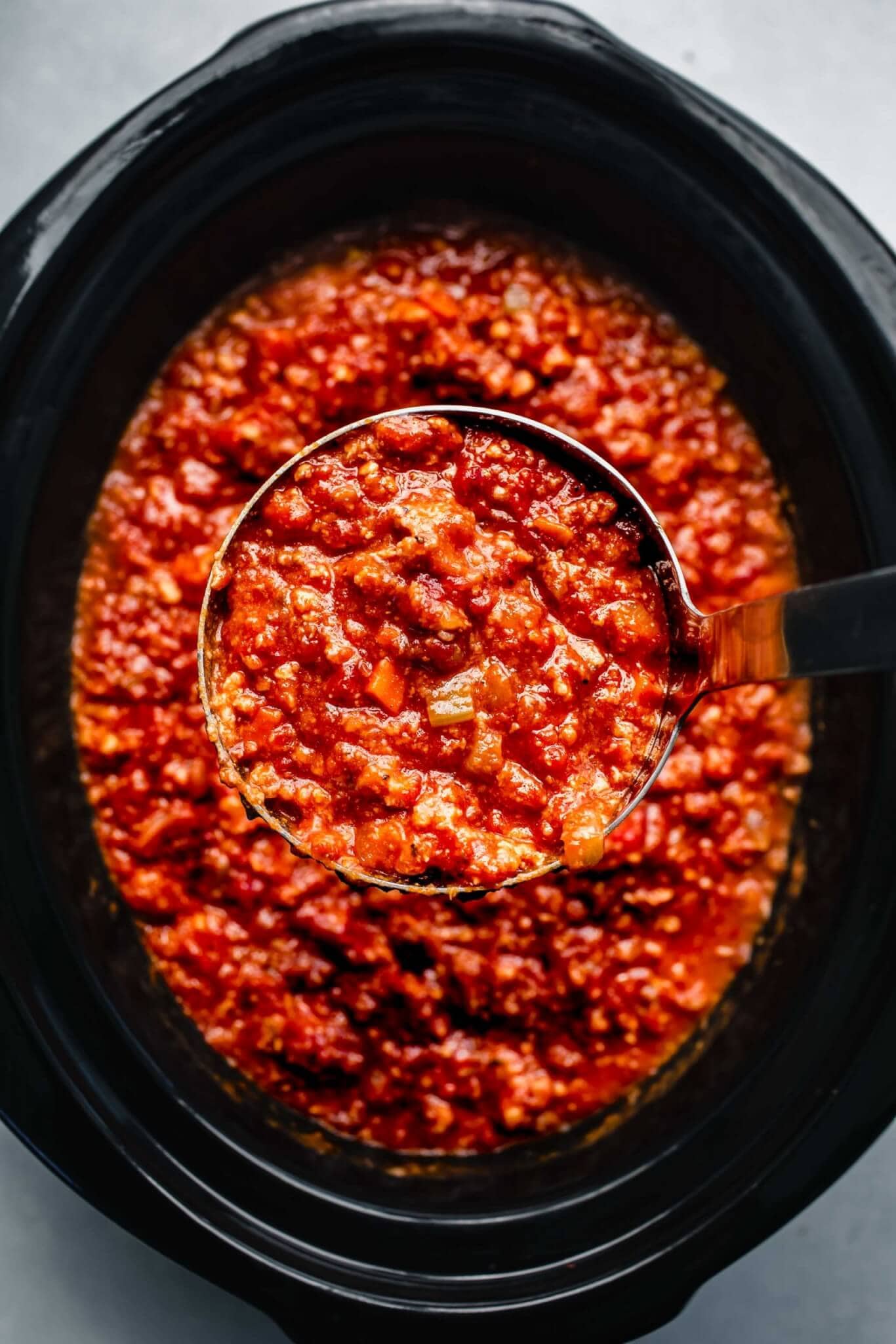 Bolognese sauce in slow cooker with ladle.