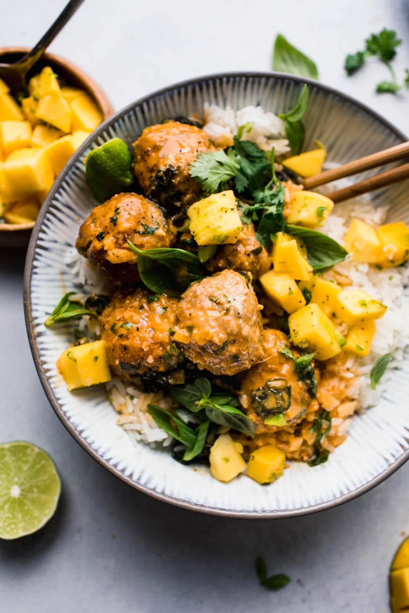 Overhead shot of curry meatballs in grey bowl with chopsticks, topped with spicy mangoes. 