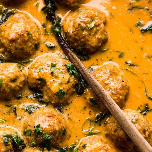 Meatballs simmering in curry sauce in skillet.