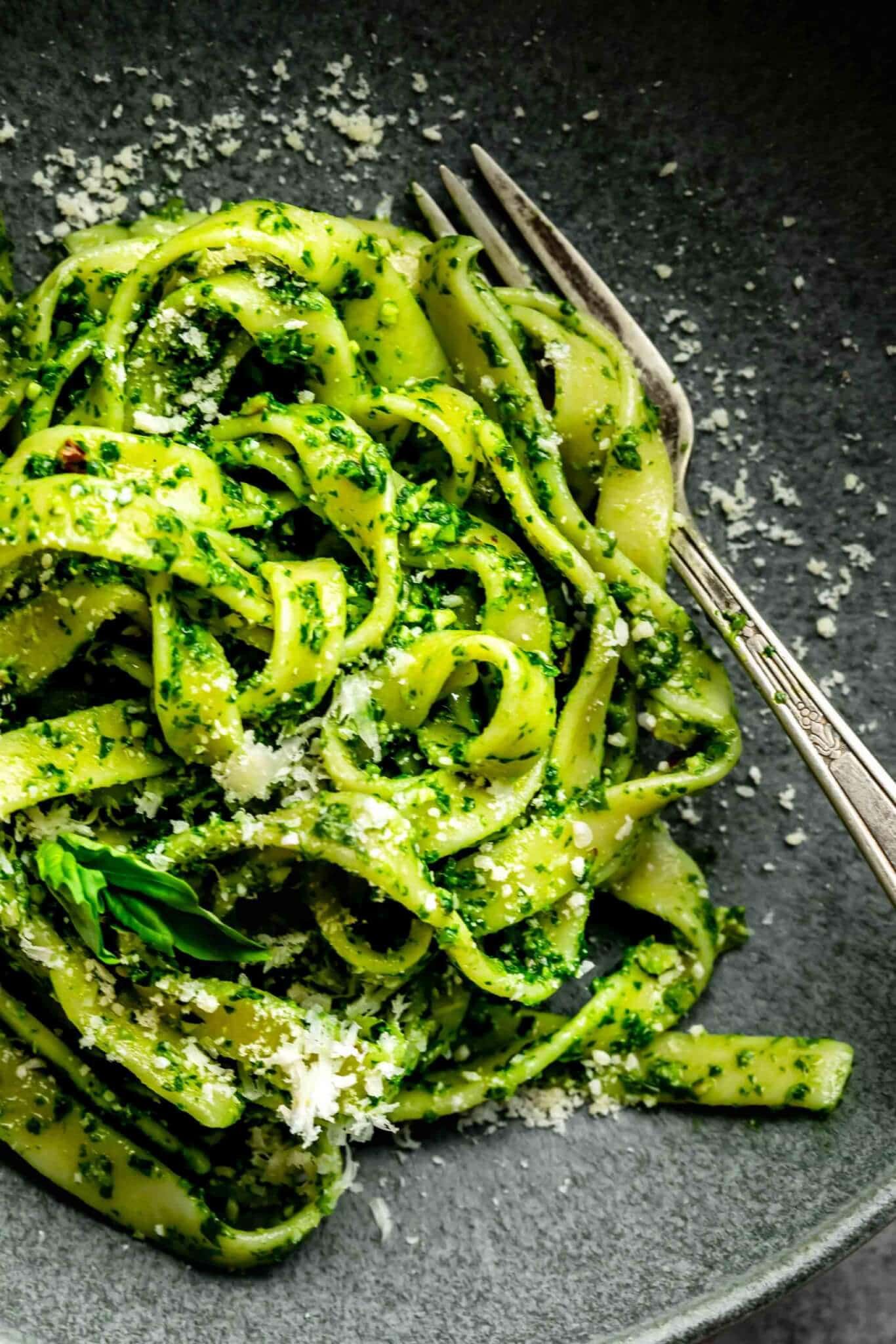 CLOSE UP OF KALE PESTO TOSSED WITH PASTA AND SPRINKLED WITH PARMESAN