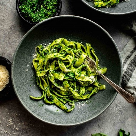KALE PESTO TOSSED WITH PASTA AND SERVED IN DARK GREY BOWL WITH FORK.