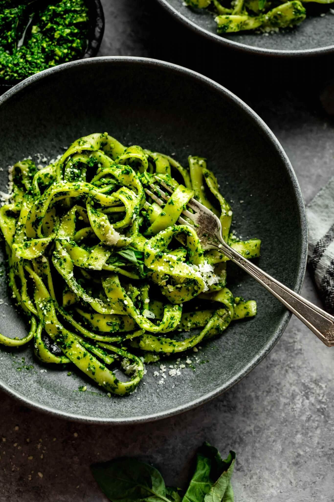 KALE PESTO TOSSED WITH PASTA AND SERVED IN DARK GREY BOWL WITH FORK.