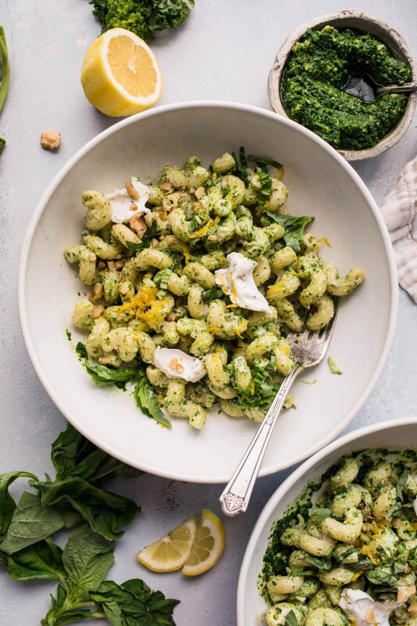 Overhead shot of pesto goat cheese pasta in white bowl next to small bowl of pesto.