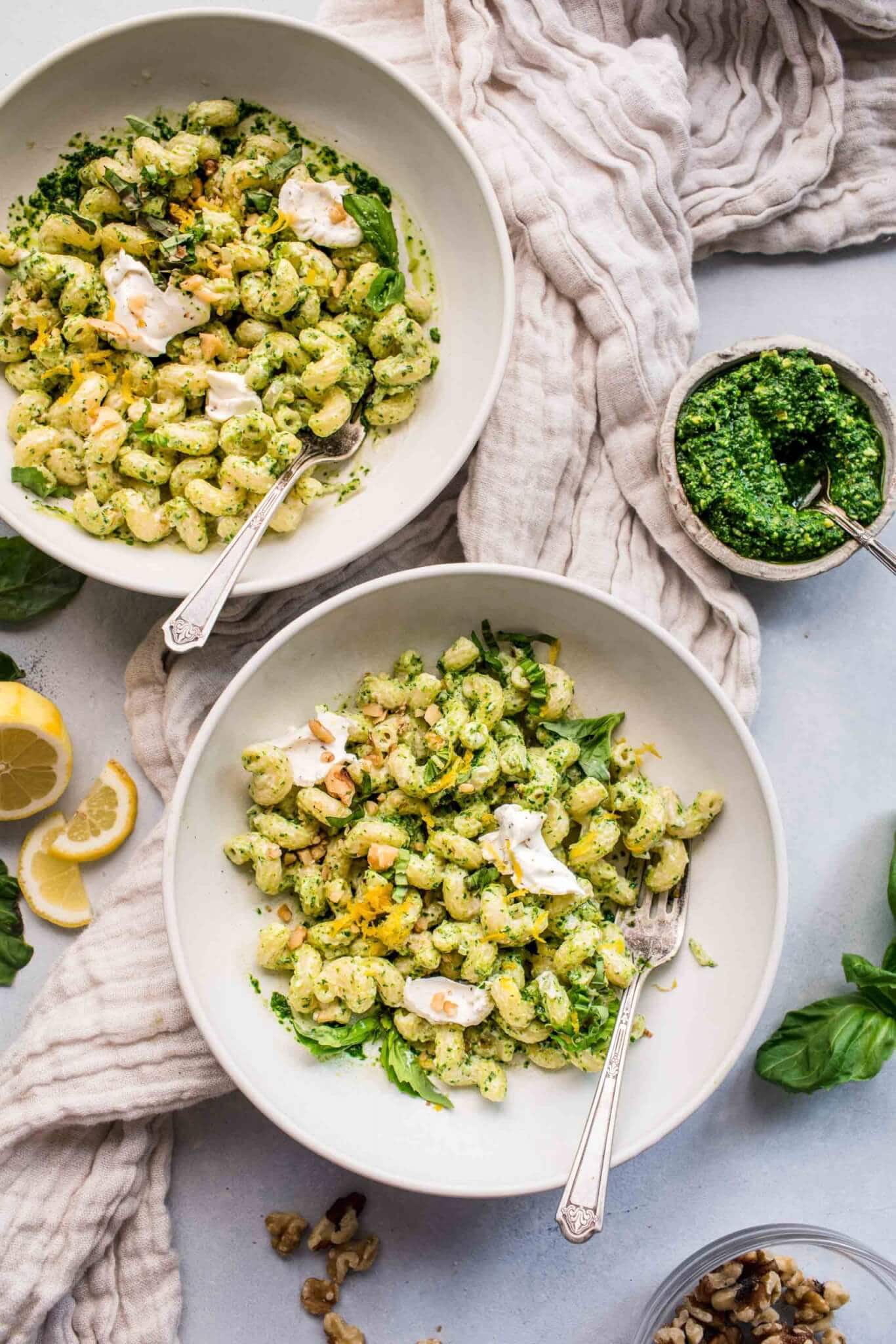 Two bowls of goat cheese pasta next to small bowl of kale pesto. 