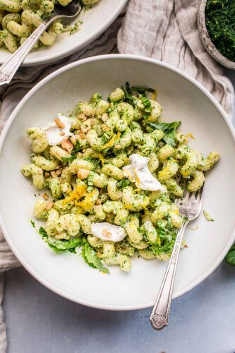Bowl of goat cheese pasta tossed with kale pesto and topped with dollops of goat cheese.