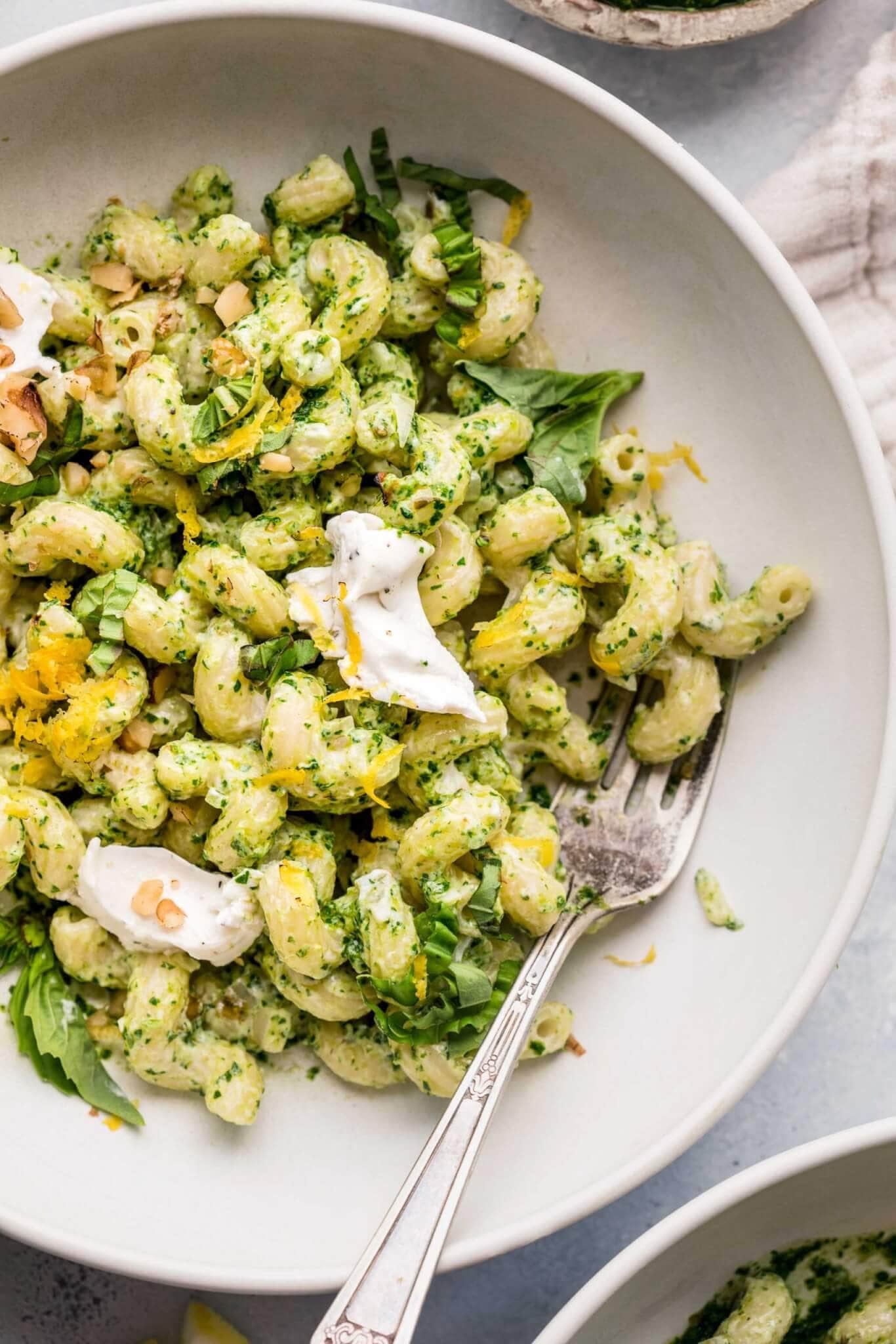 Bowl of goat cheese pasta tossed with kale pesto and topped with dollops of goat cheese.