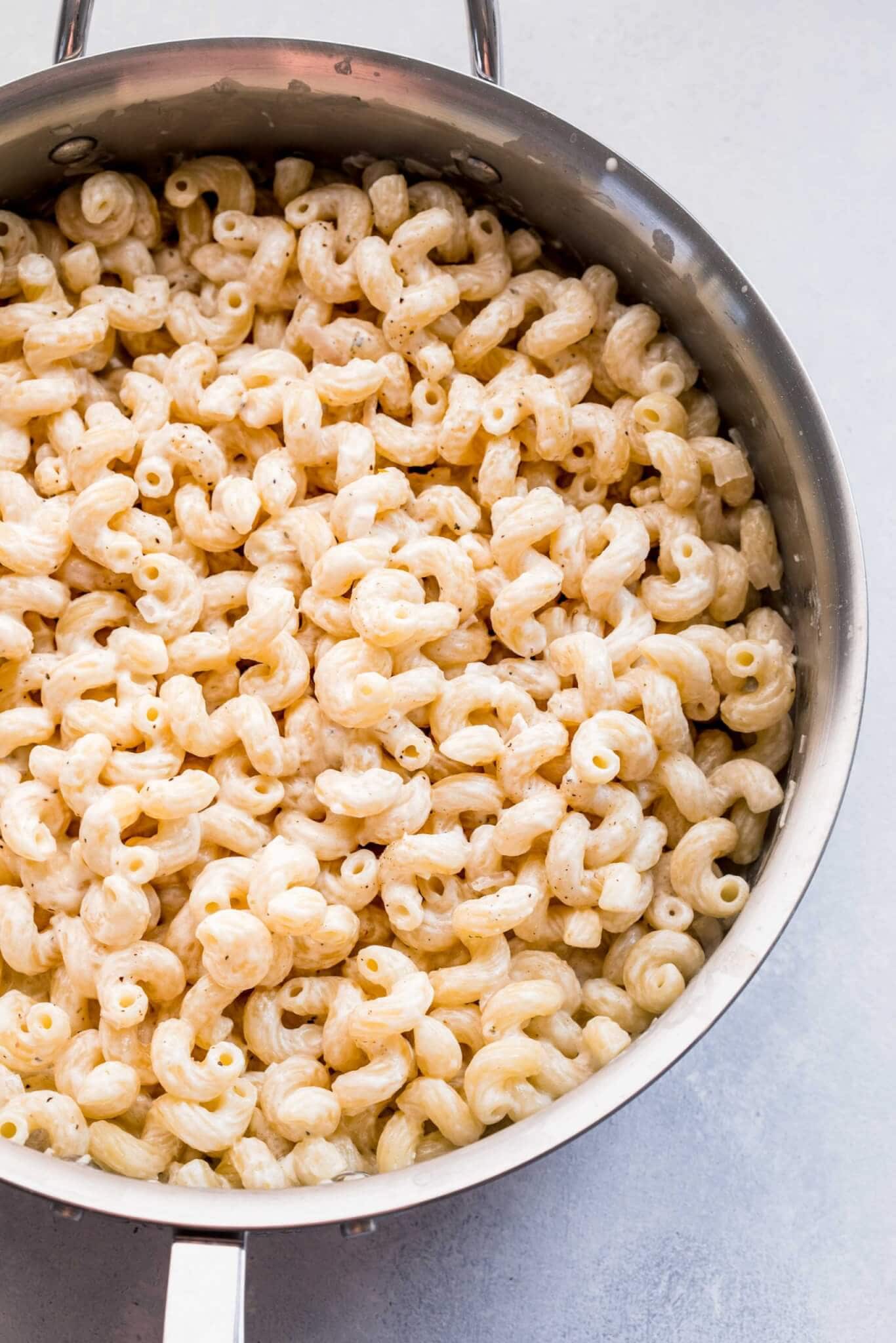 Skillet of cooked pasta tossed with goat cheese.