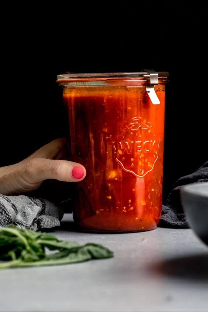 Hand holding jar of homemade marinara sauce.