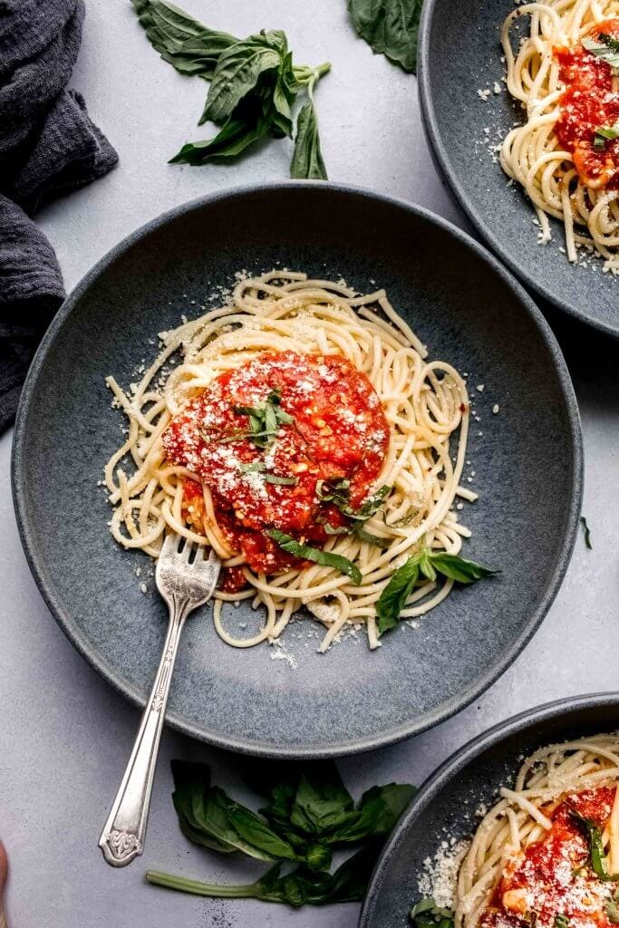 Spaghetti topped with marinara sauce in grey bowl with fork.