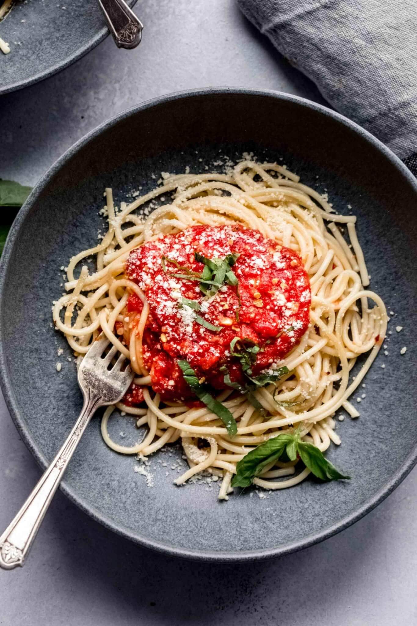 Spaghetti topped with marinara sauce in grey bowl with fork.
