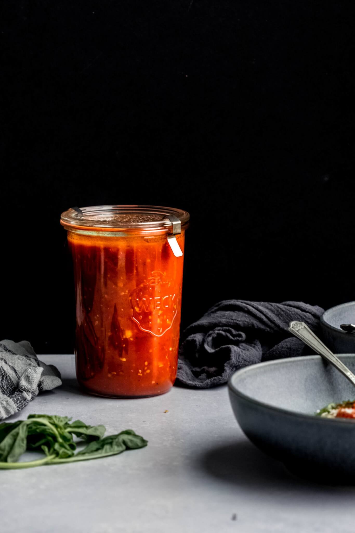 Jar of homemade marinara sauce against black backdrop. 