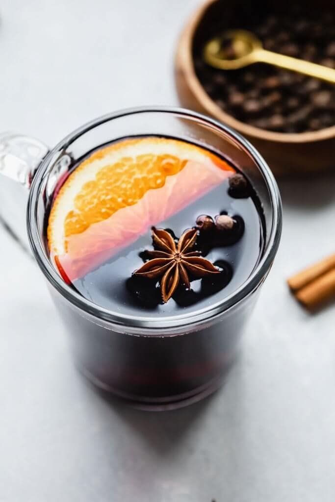 Three mugs of mulled wine on counter next to cinnamon sticks and orange slices.