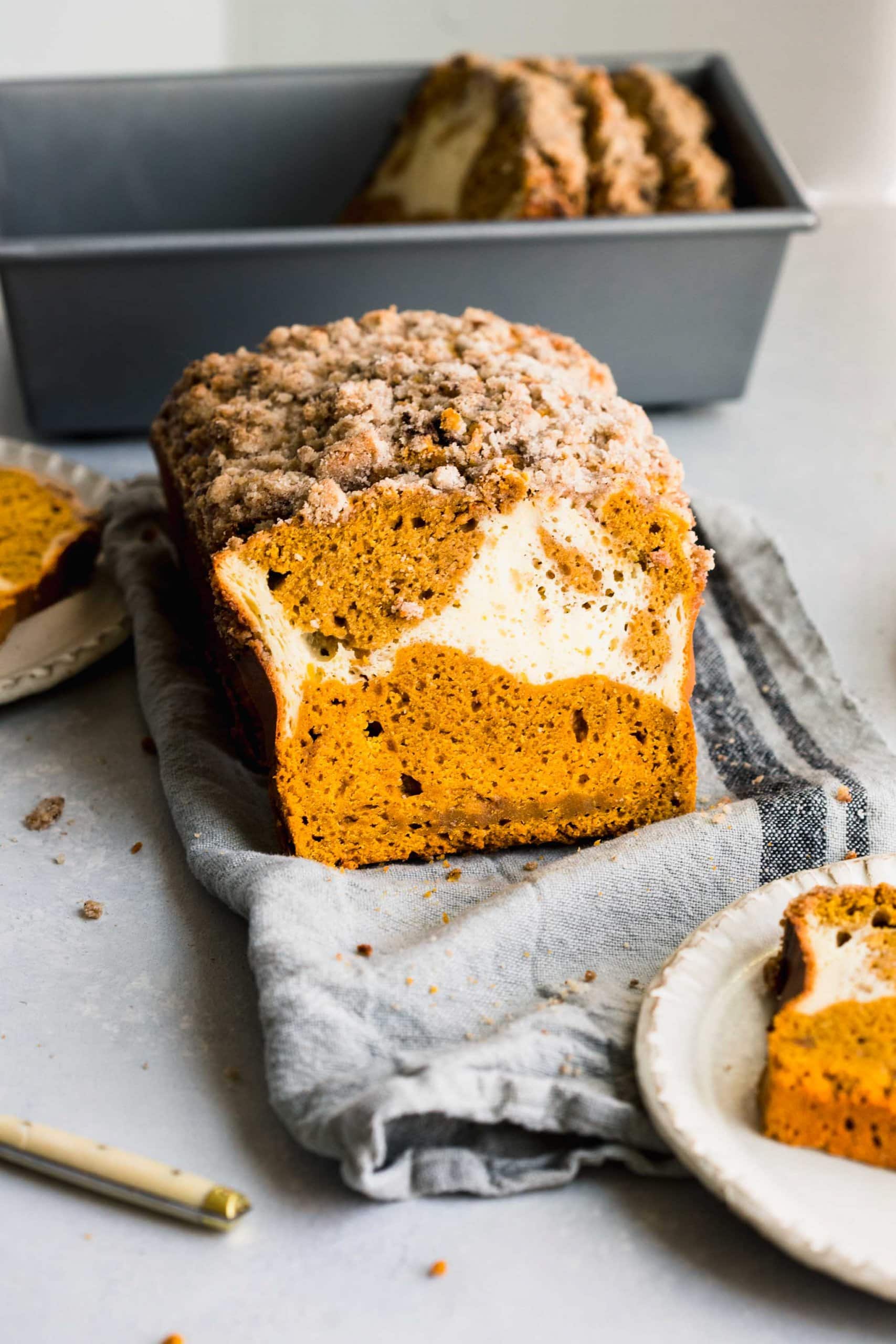 Side view of loaf of pumpkin bread cut into with cream cheese swirl showing.