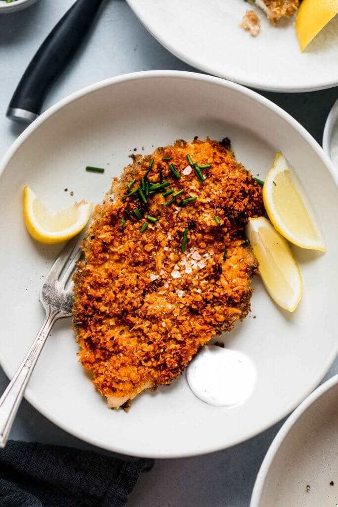 Crispy baked chicken in shallow white bowl with dollop of sour cream.