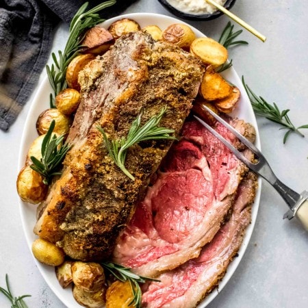 Sous vide prime rib arranged on platter with roasted potatoes and rosemary sprigs.