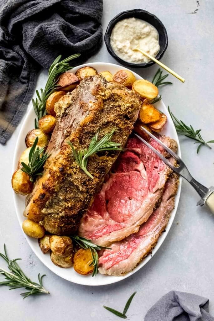 Sous vide prime rib arranged on platter with roasted potatoes and rosemary sprigs.