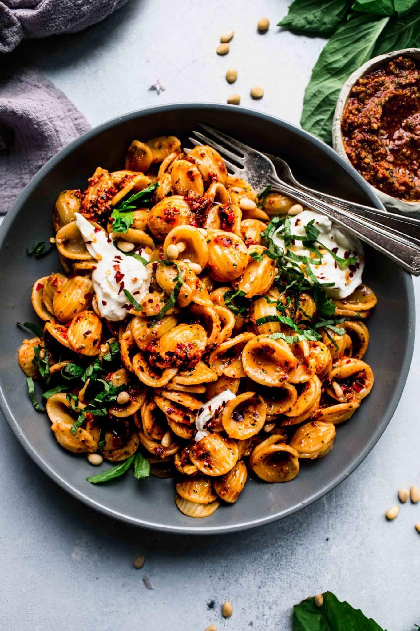 Sun dried pesto tossed with pasta and served in grey bowl with burrata cheese.