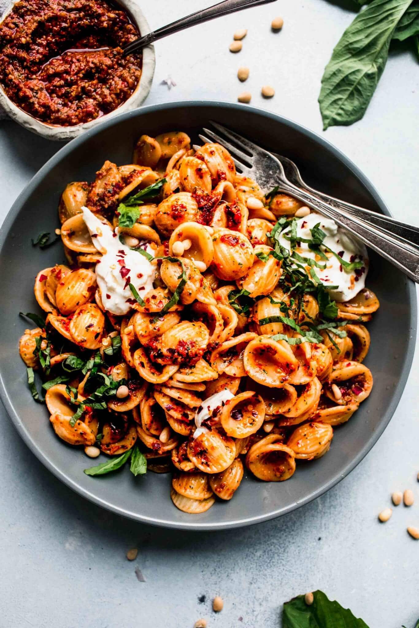 Sun dried pesto tossed with pasta and served in grey bowl with burrata cheese.