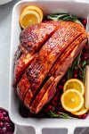 Glazed ham in roasting dish garnished with oranges, cranberries and herbs.