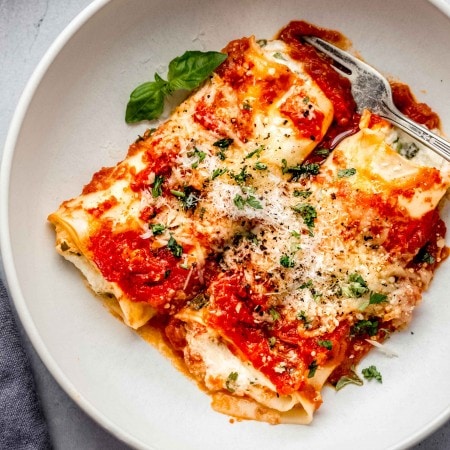 Two manicotti in white bowl topped with parsley.