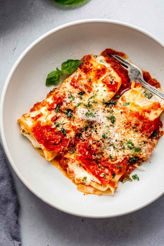 Two manicotti in white bowl topped with parsley.