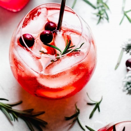 Winter aperol spritz garnished with cranberries and rosemary.