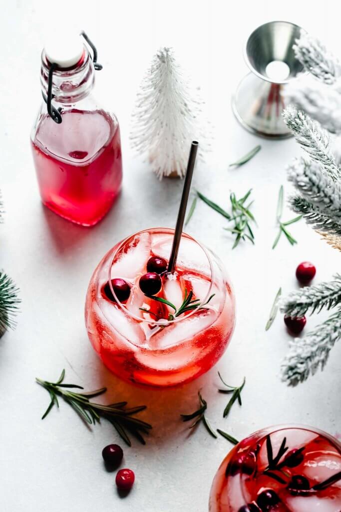Winter aperol spritz cocktail next to small bottle of cranberry simple syrup. 
