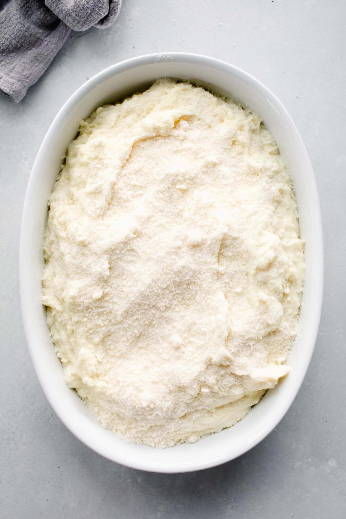 Unbaked mashed potatoes in casserole dish topped with parmesan.