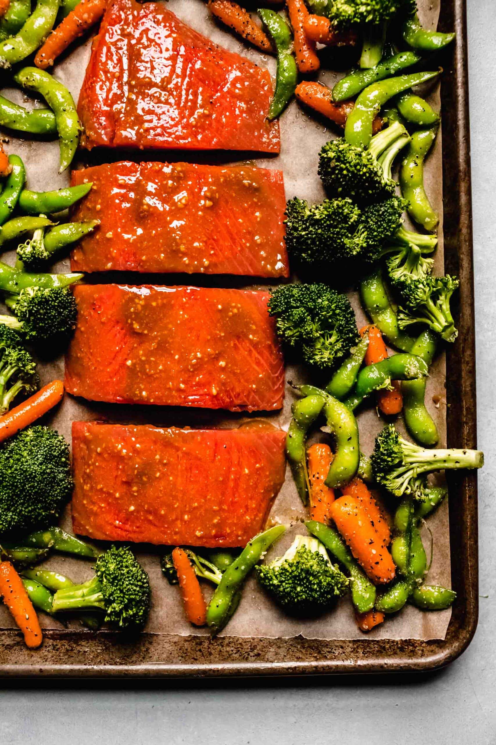 Salmon brushed with miso glaze and vegetables on baking sheet.