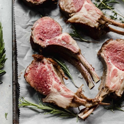 Rack of lamb sliced into chops and laid out on tray next to fresh herbs.