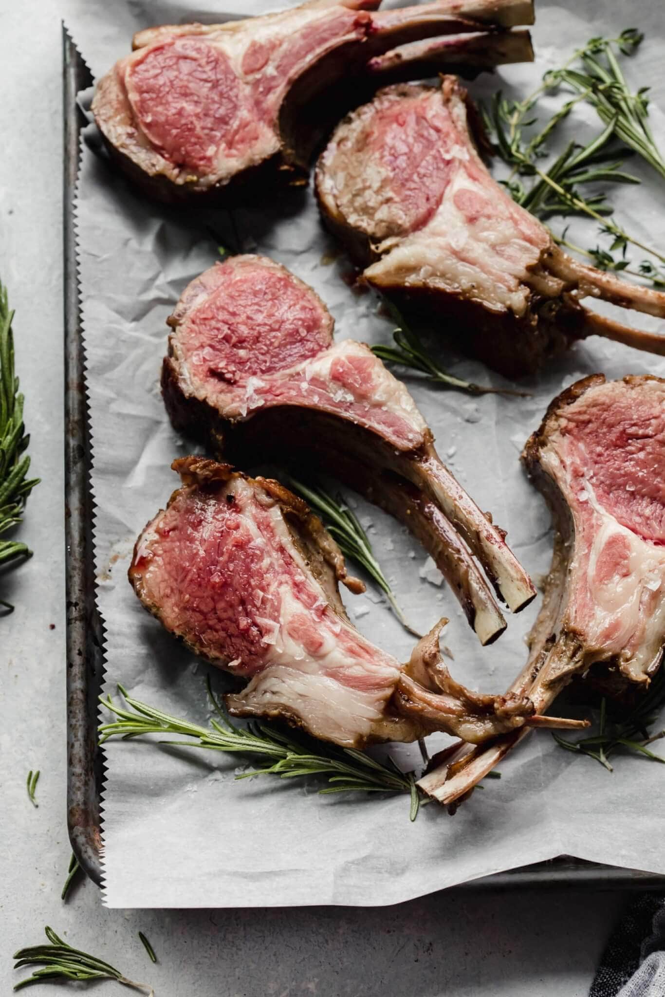 Rack of lamb sliced into chops and laid out on tray next to fresh herbs.