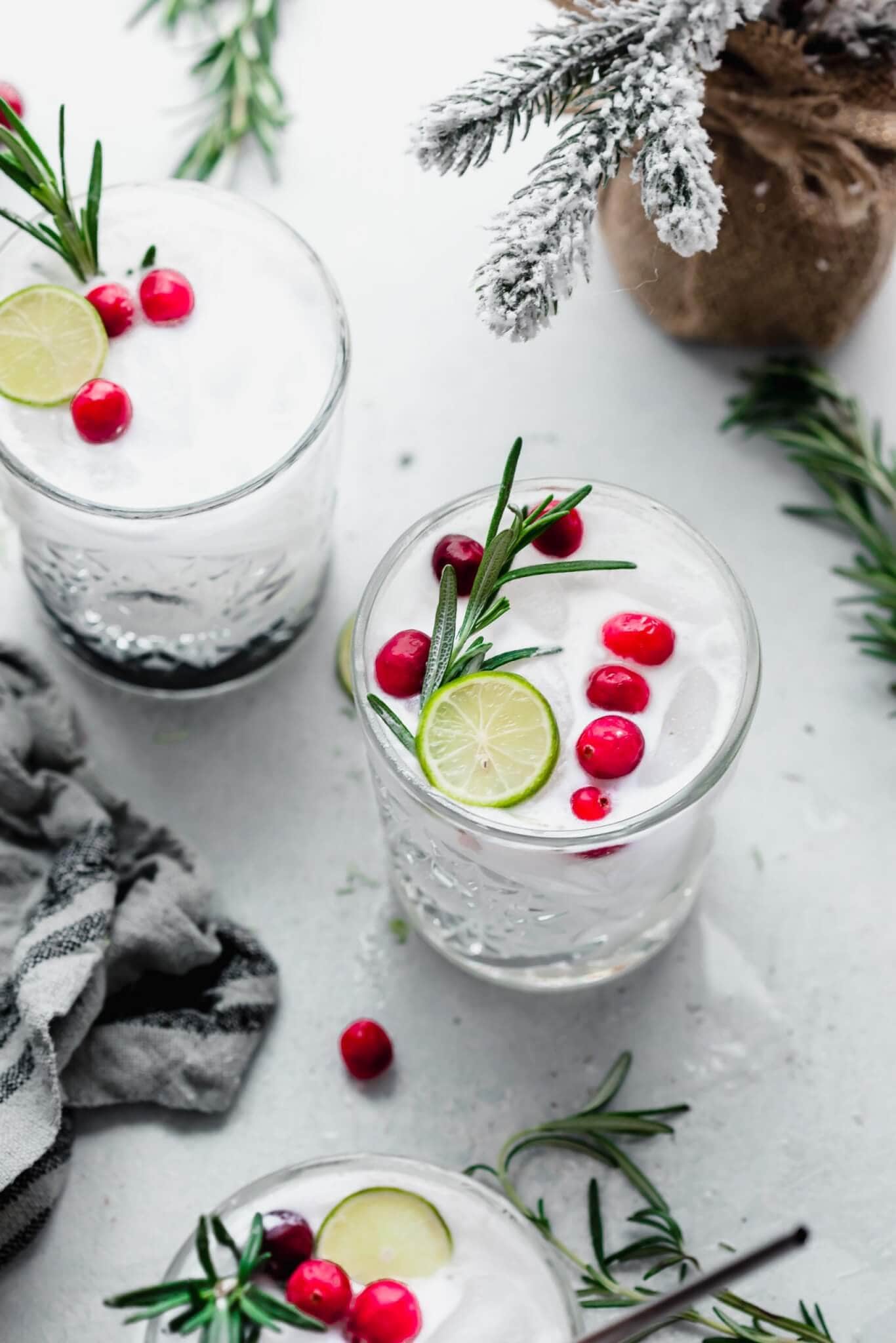 Three Christmas margaritas on counter with gray towel, fresh cranberries, and rosemary sprigs. 