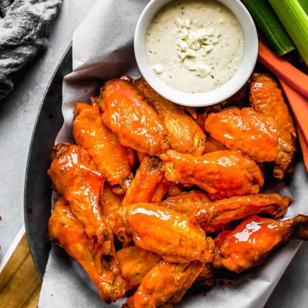 Air fryer wings in serving basket with blue cheese and celery sticks.