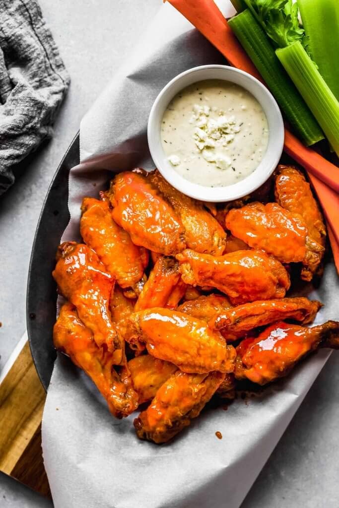 Air fryer wings in serving basket with blue cheese and celery sticks.