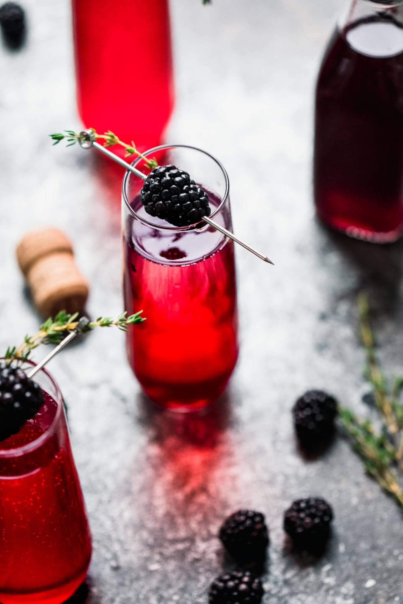 Shot of blackberry champagne cocktail garnished with blackberry and thyme sprig.