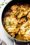 French onion chicken in skillet with spoon.