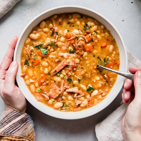 Bowl of Slow Cooker Ham and Bean Soup with hands holding bowl and spoon