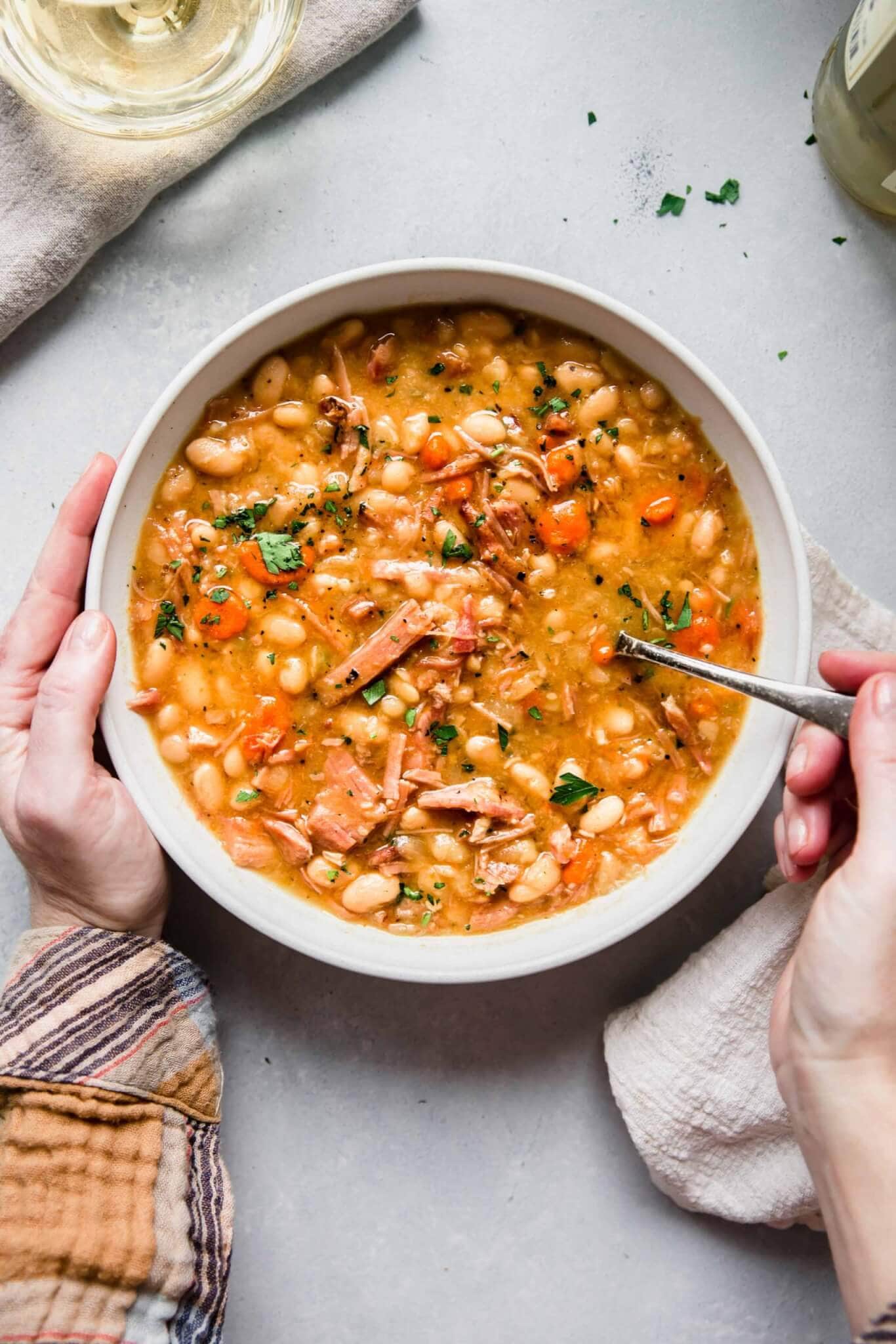 Bowl of Slow Cooker Ham and Bean Soup with hands holding bowl and spoon