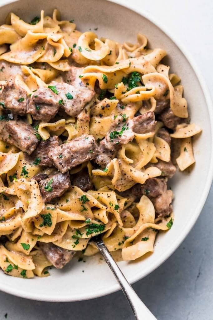 Beef stroganoff in large white bowl with serving spoon. 
