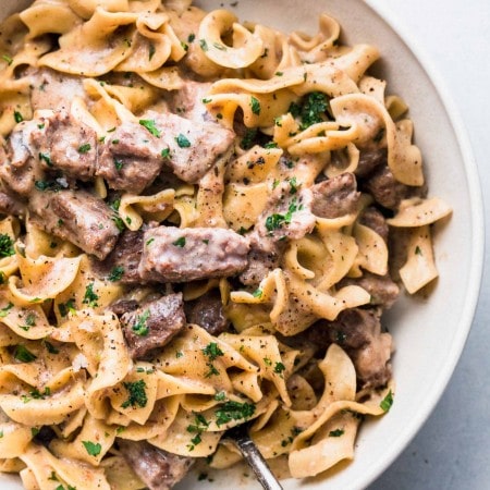 Beef stroganoff in large white bowl with serving spoon.